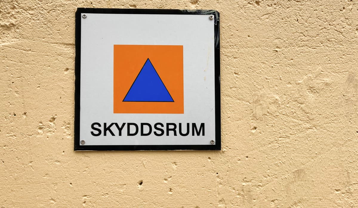 Skylt för hänvisning till skyddsrum som sitter på en gul vägg. 