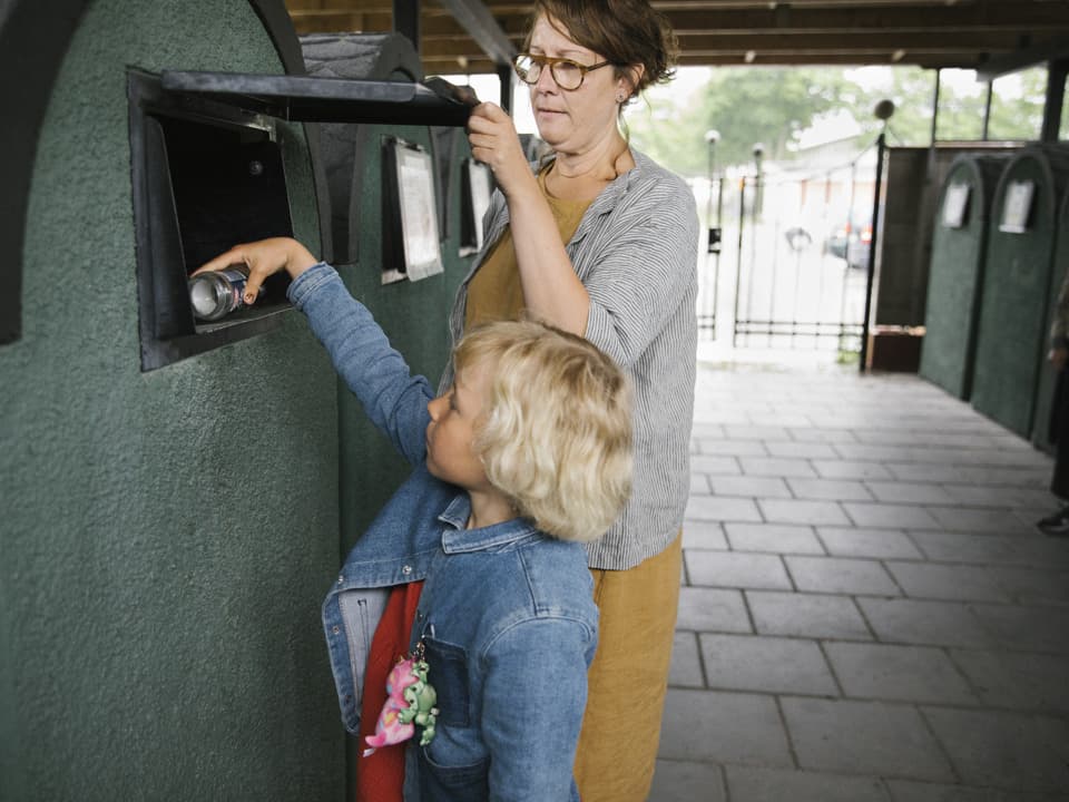 En kvinna och en flicka slänger sopor i ett miljöhus.