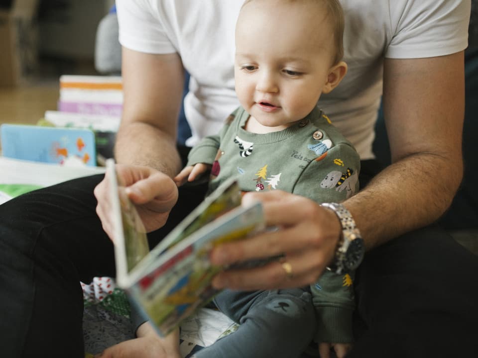 Ett barn sitter i knä på en vuxen och bläddrar i en bok.