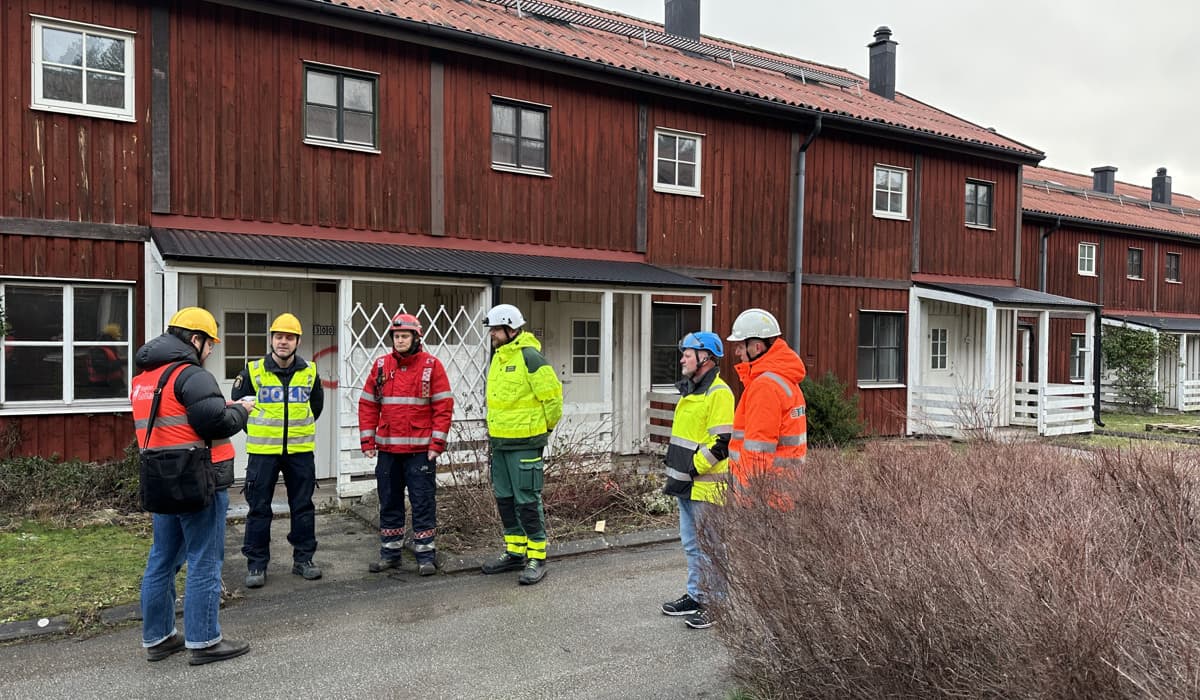 Män med gula varselkläder framför ett rött trähus