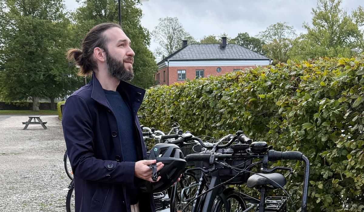 En man som står vid en lådcykel och håller en hjälm i händerna.