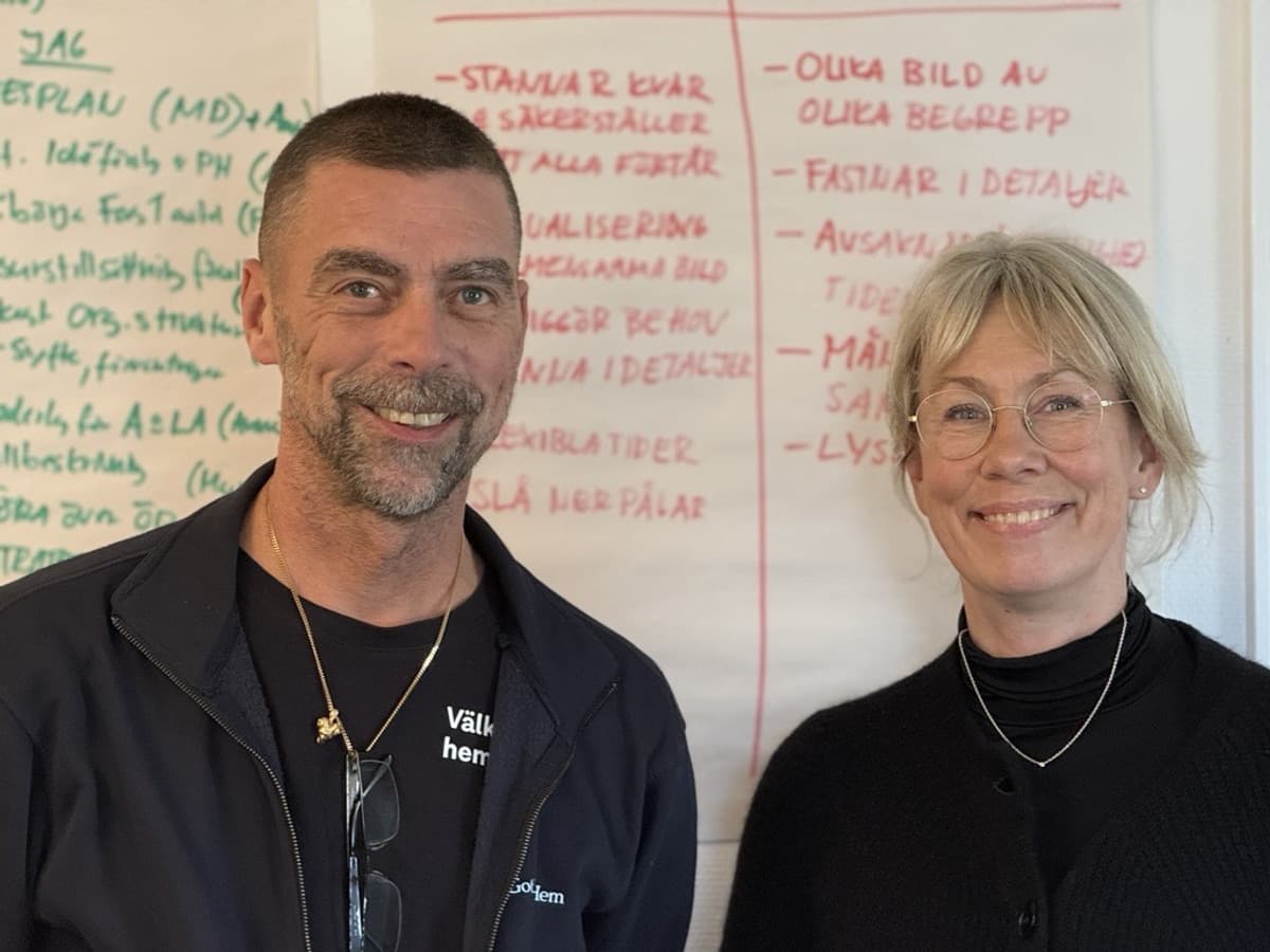 En man och en kvinna i mörka kläder ser in i kameran och ler.