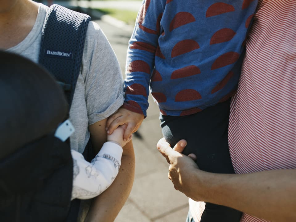 Två barn håller hand medan de sitter i famnen på varsin vuxen. De är utomhus.