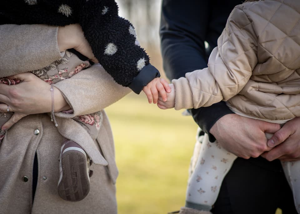 Två små barn som håller hand i två vuxnas famn