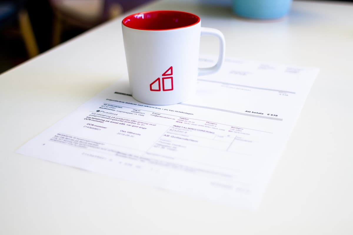 En vit kopp med röd GotlandsHem logga står på en hyresavi i pappersformat. Pappret ligger på ett vitt bord.