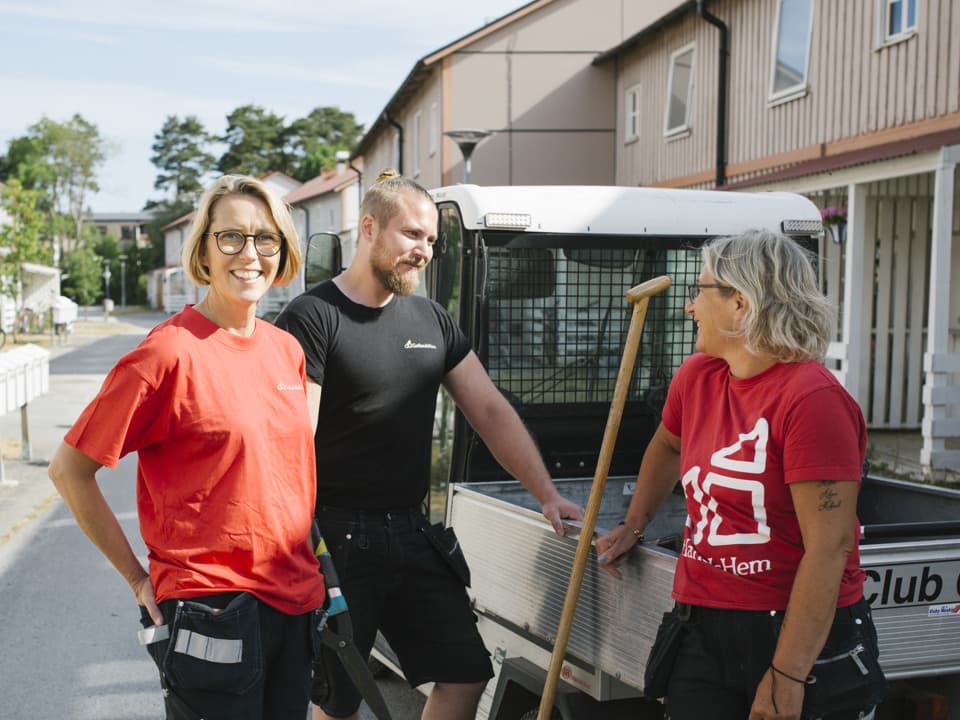 Två kvinnor och en man står vid en golfbil i ett bostadsområde. Kvinnorna har röda t-shirts på sig och mannen har en svart t-shirt. Alla tre har svarta arbetsbyxor.