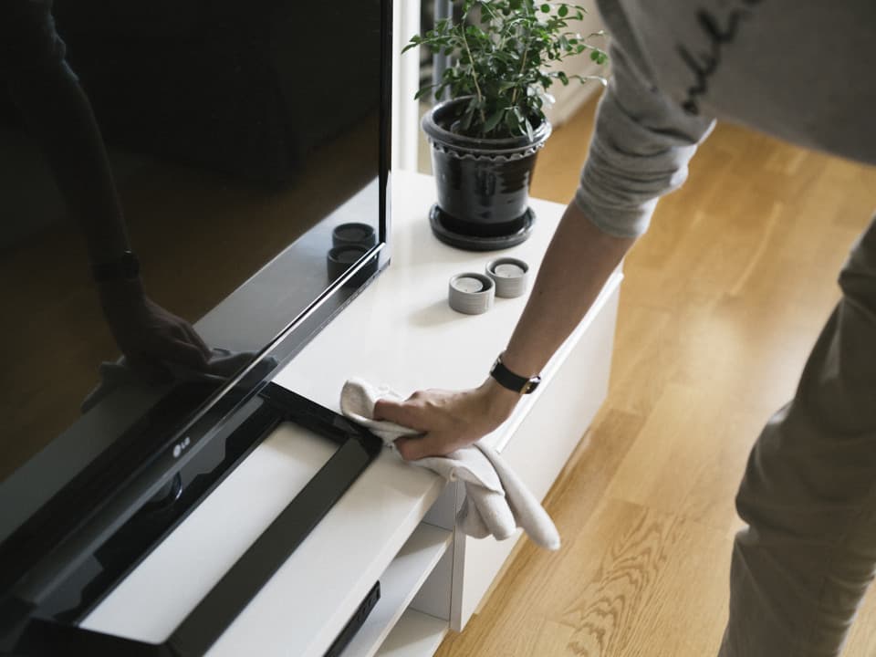 En person torkar med en trasa på en tv-bänk.