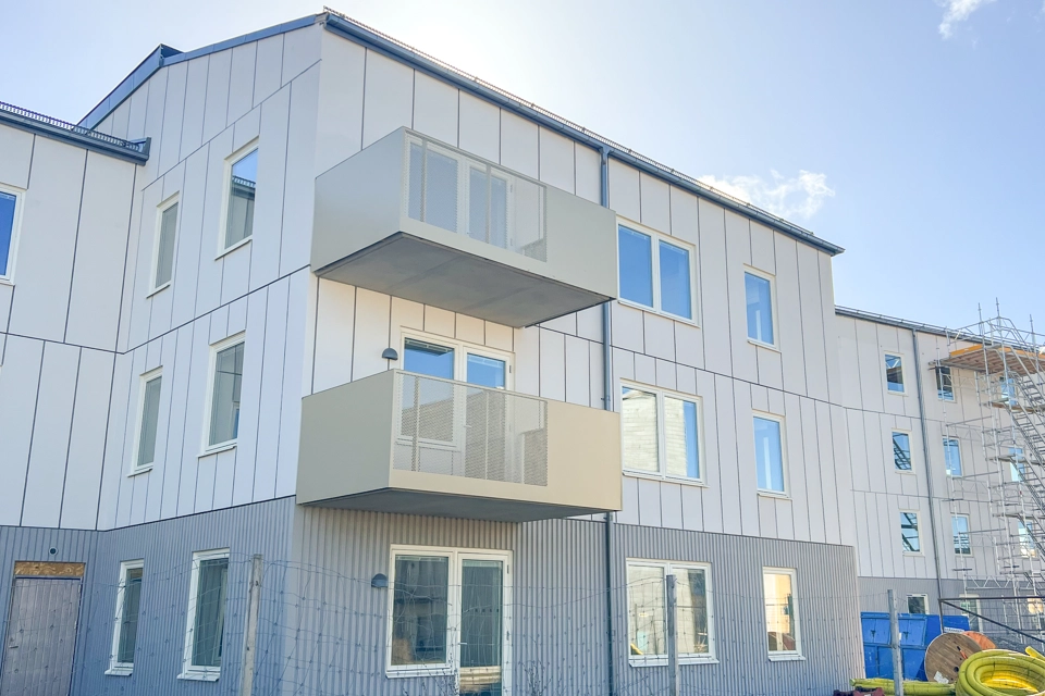 Flerbostadshus med vit fasad och gula balkonger. Klarblå himmel. 