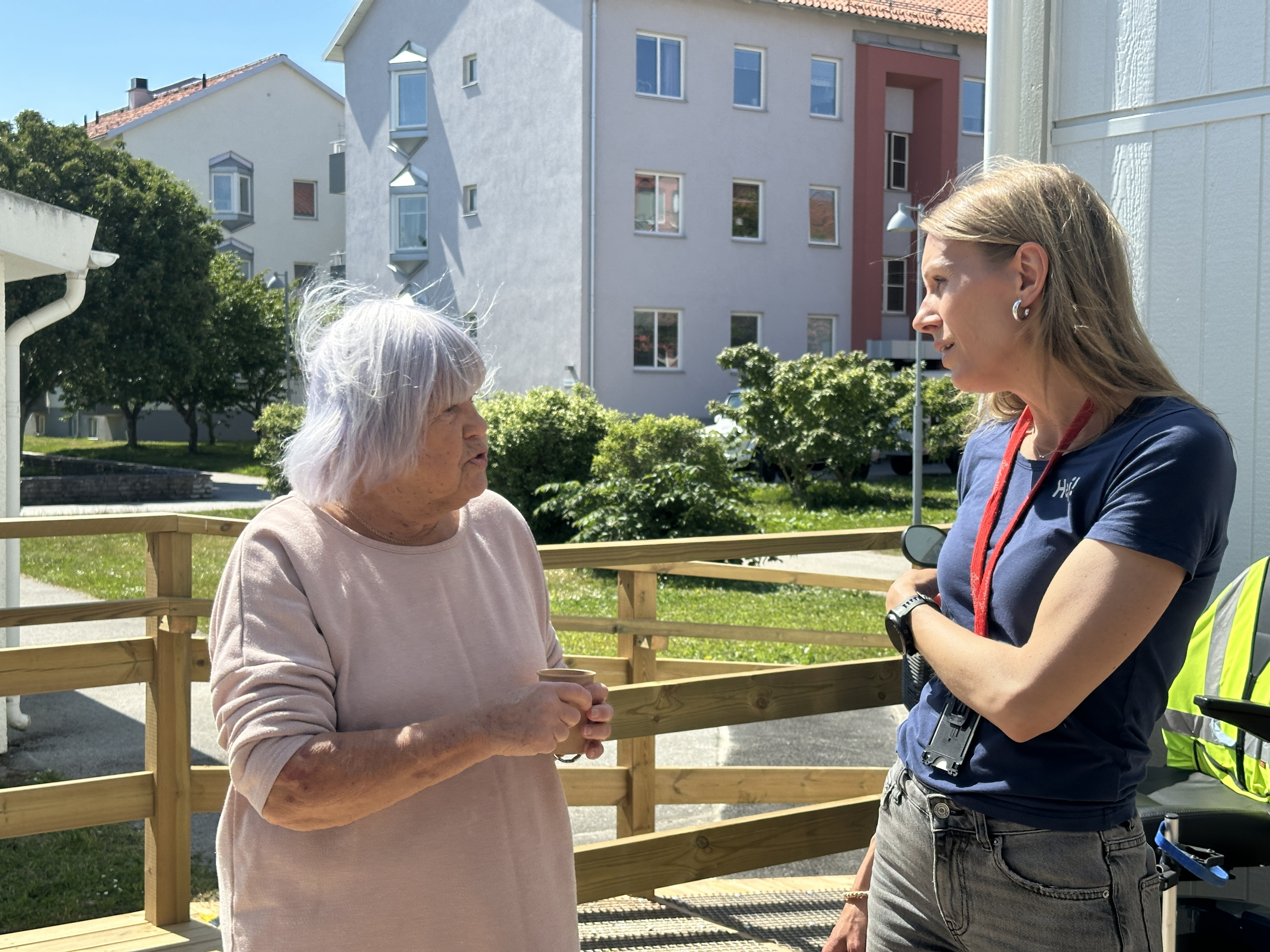 En medarbetare på GotlandsHem står och pratar med en äldre kvinna. Solen skiner och det är sommar.