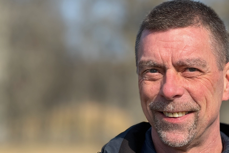 En man i blå jacka ler mot kameran.