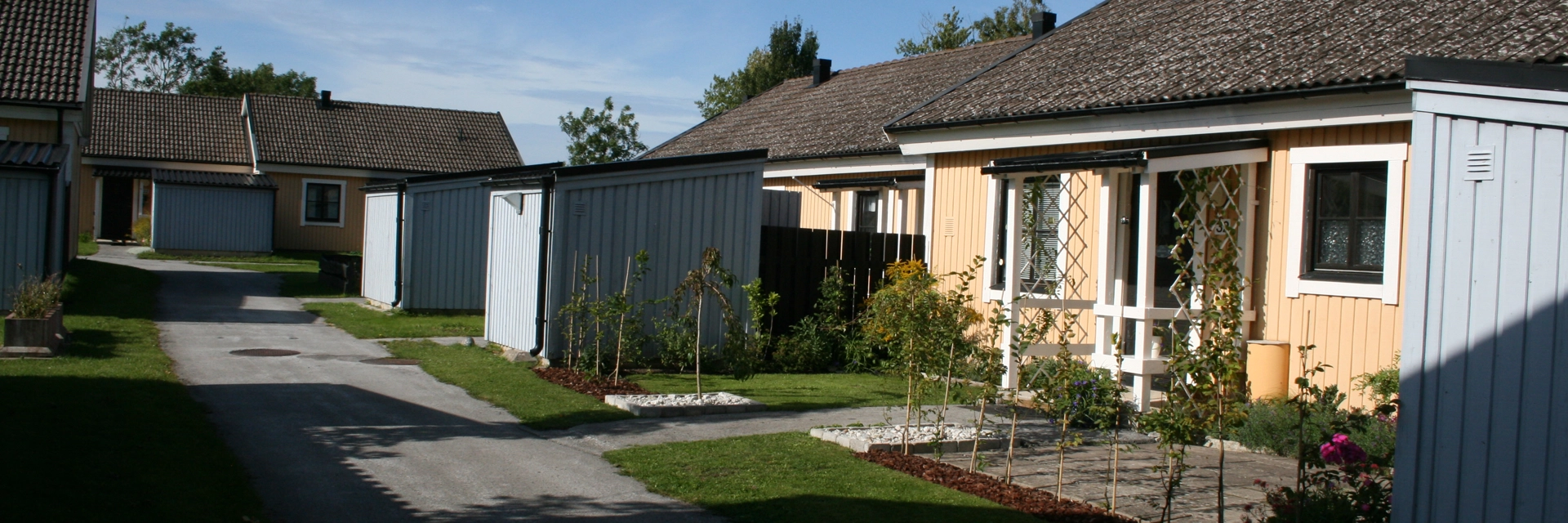 Gula radhus med vita knutar och separata ljusblå förråd. Himlen är blå med ett fåtal moln.