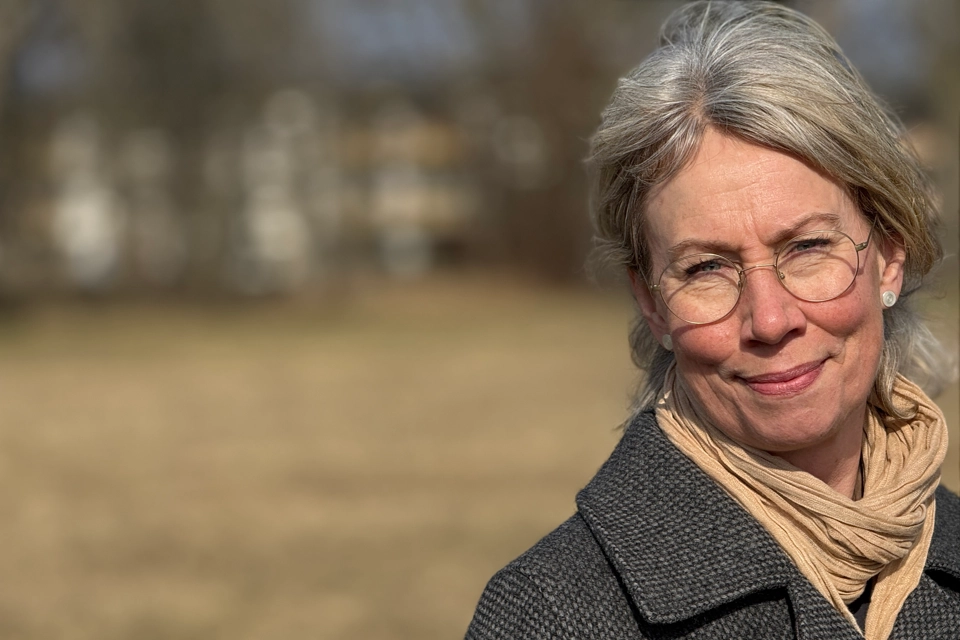 En kvinna i kappa och halsduk står på ett fält.