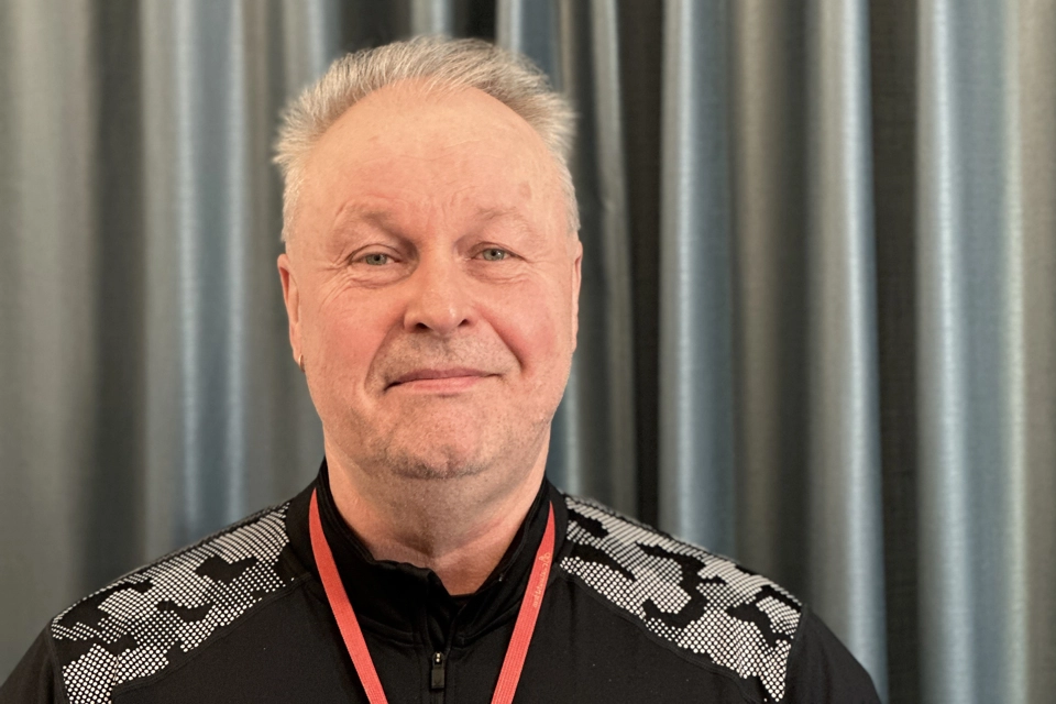 En man står framför en gardin och ler mot kameran.