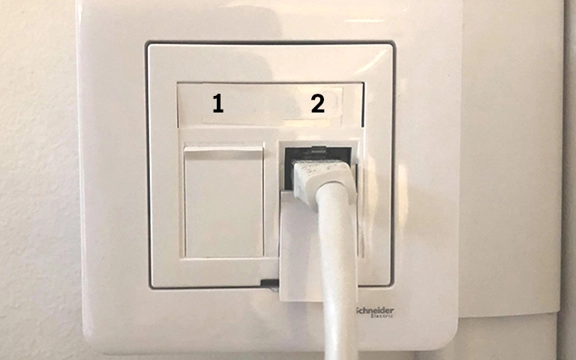 Ett bredbandsuttag på en vit vägg. Det finns två uttag och en kabel sitter i det ena uttaget.