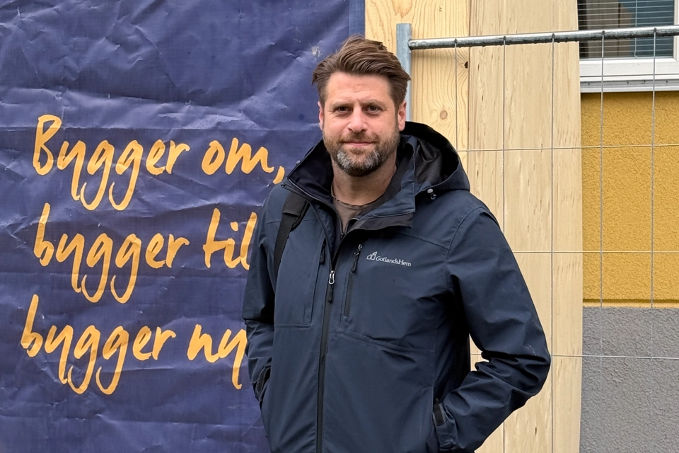En man som står framför en byggskylt som står "Bygger om, bygger till, bygger nytt" på.