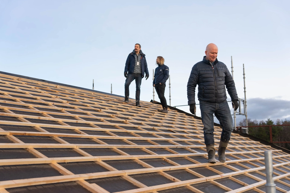 Tre män står på en krönet av ett tak som håller på att byggas. En av dem är Joakim Martell och han går mot kameran.