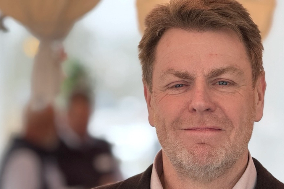 En välklädd man med kort hår och skägg ser in i kameran och ler.