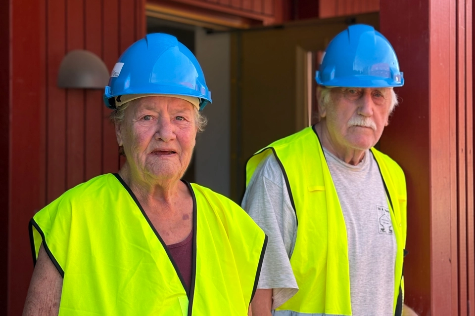 Två äldre personer som bär skyddshjälmar och säkerhetsvästar.