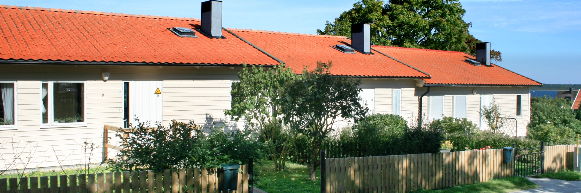 Bostadsområde Fårösund, vita enplan radhus. Framför husen är gräsmatta, buskar och staket. Himlen är blå.