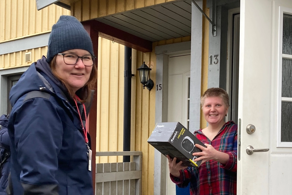 En servicevärd  (numera ombyggnadssamordnare) från GotlandsHem har lämnat över en värmefläkt till en hyresgäst i Fårösund. De står vid en öppen dörr till ett gult hus.