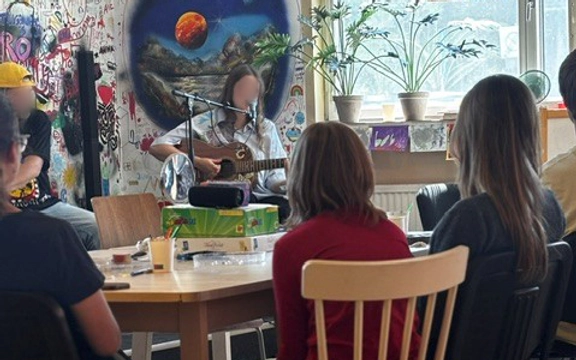 En grupp människor som sitter och tittar på en person som spelar gitarr.