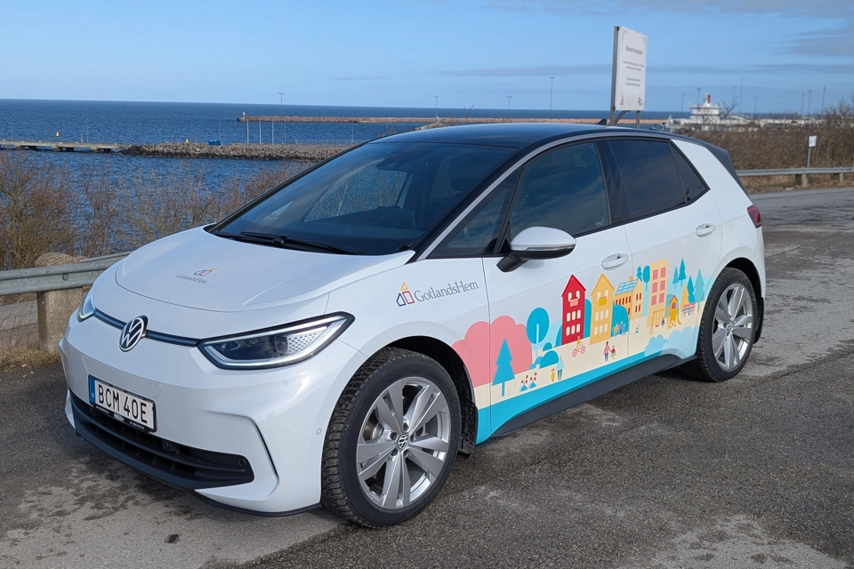 En vit bil med en hamn i bakgrunden