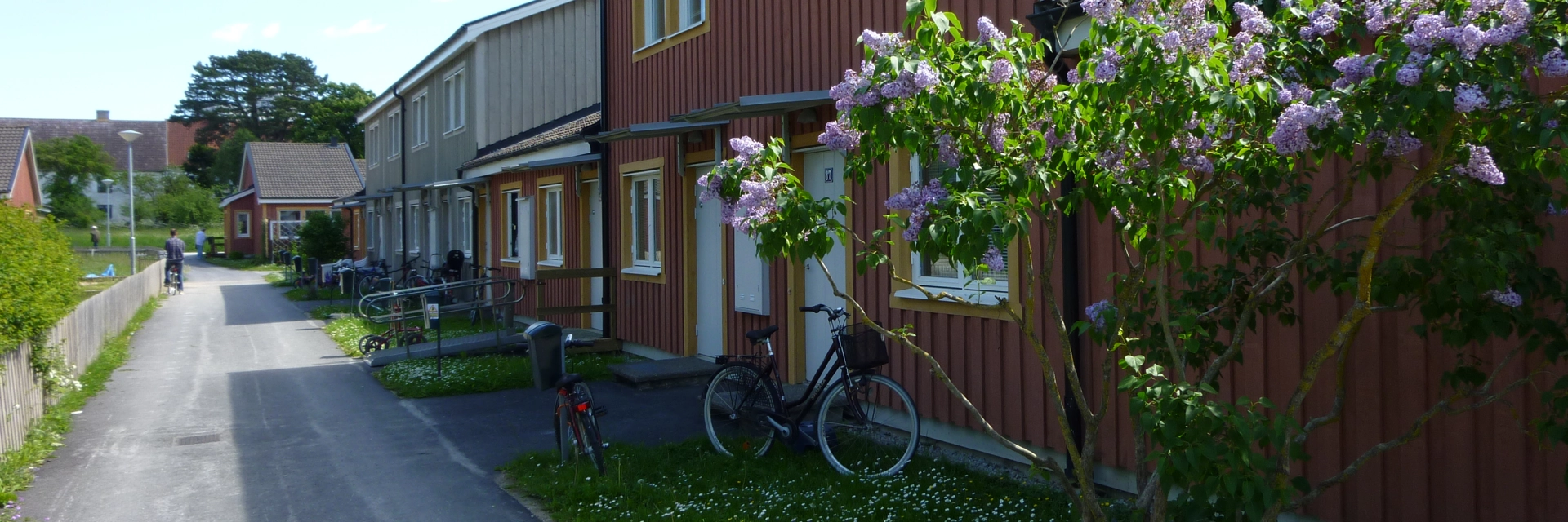 Rött trähus med gula knutar. Framför huset är en gräsplätt och därefter gång- och cykelväg.