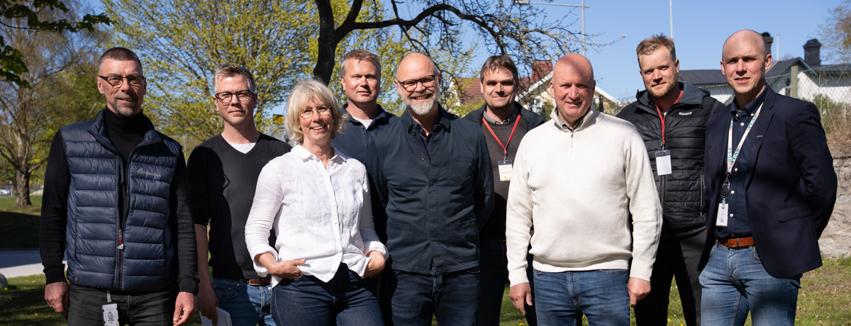 En grupp med människor på en gräsmatta i vår solen. De ser alla in i kameran och ler.