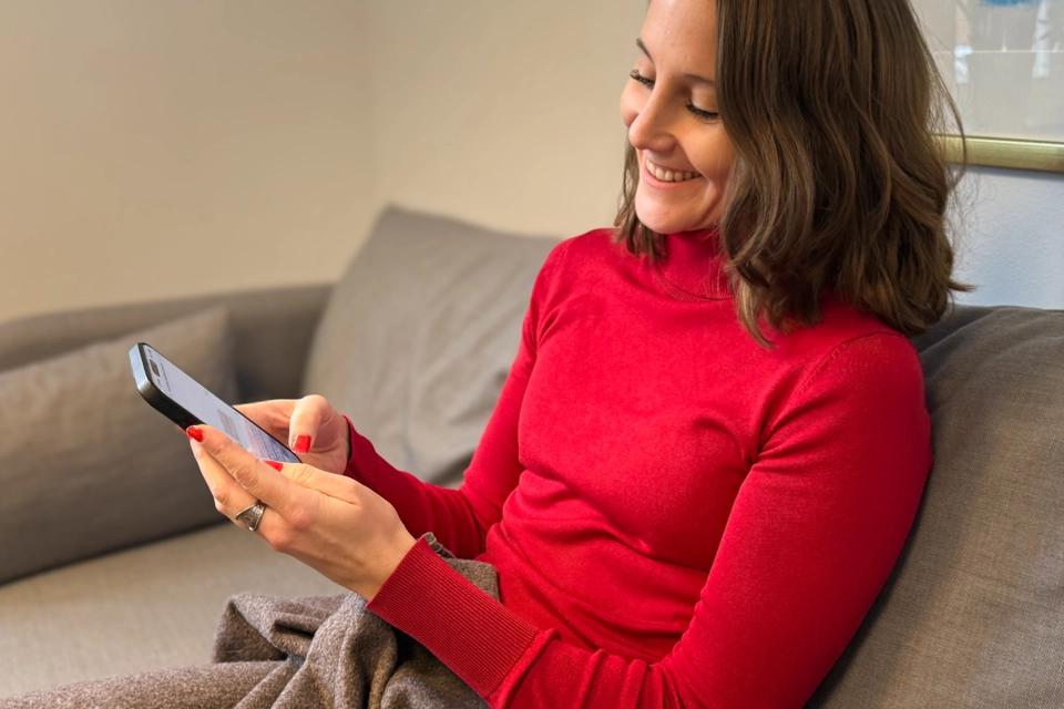 En kvinna sitter i en soffa och surfar nöjt på en mobiltelefon.