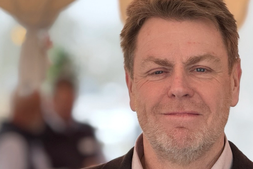 En välklädd man med kort hår och skägg ser in i kameran och ler.