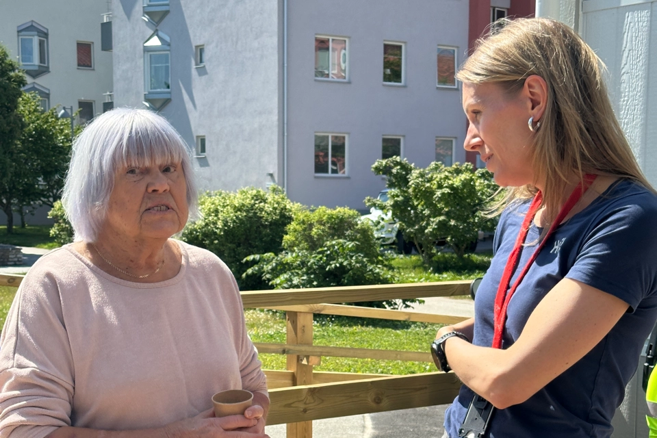 En medarbetare på GotlandsHem står och pratar med en äldre kvinna. Solen skiner och det är sommar.