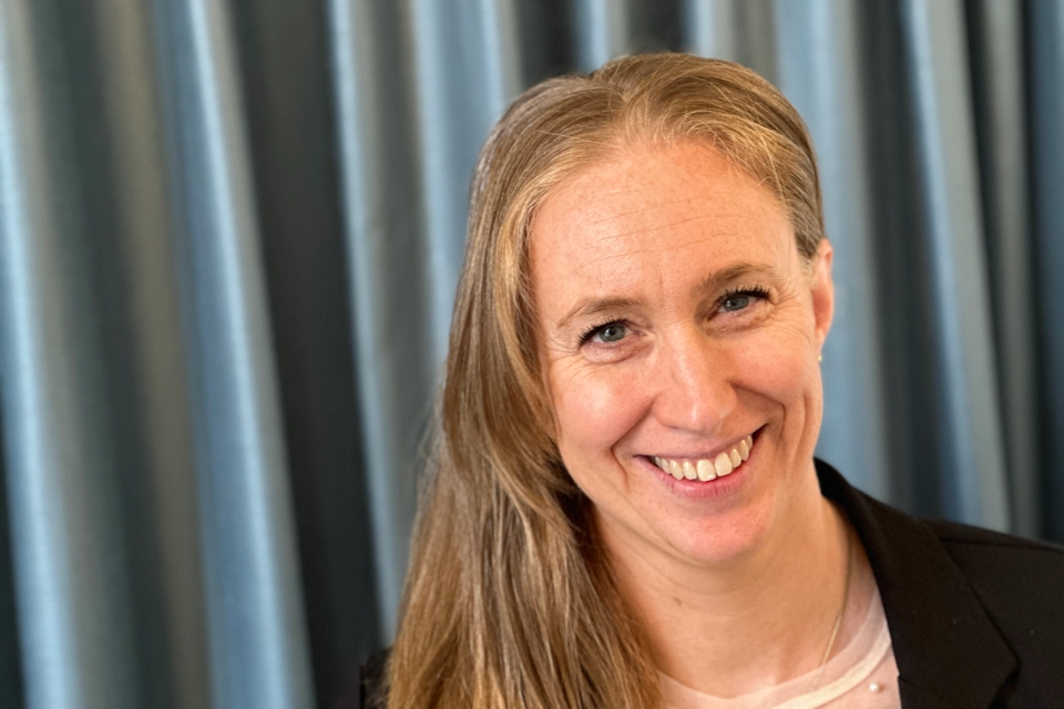 En glad kvinna med rött hår och svart kavaj ler mot kameran.