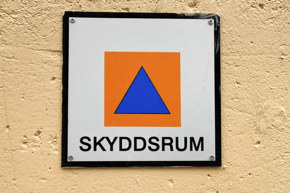 Skylt för hänvisning till skyddsrum som sitter på en gul vägg. 