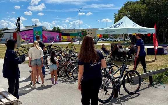 En grupp människor som står runt ett antal cyklar. Det finns ett stort blått tält som står "Gotlandshem" på.