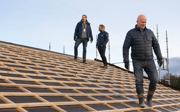 Tre män står på en krönet av ett tak som håller på att byggas. En av dem är Joakim Martell och han går mot kameran.