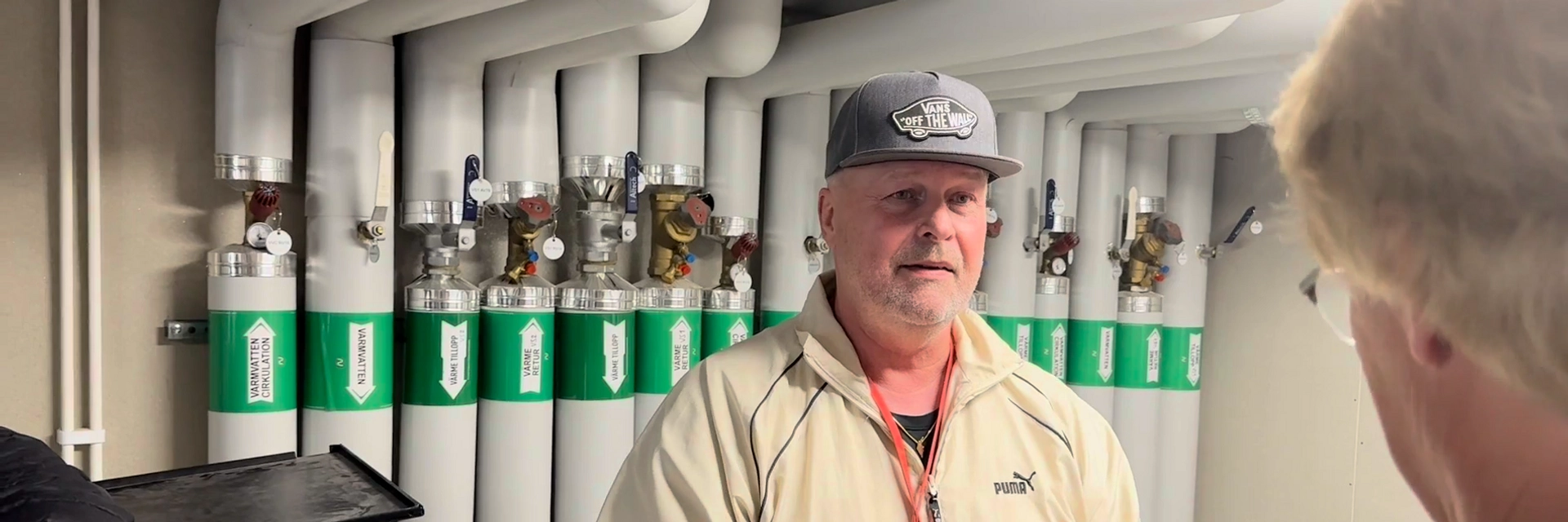 En man står framför en vägg full av rör med spakar på. Det ser ut som de står i något tekniskt utrymme i en källare.