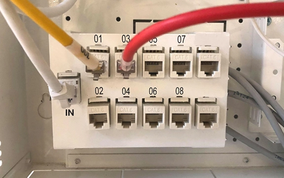 En vit uttagspanel i ett bredbandsskåp. Det är en vit, en gul och en röd sladd som sitter i panelen.