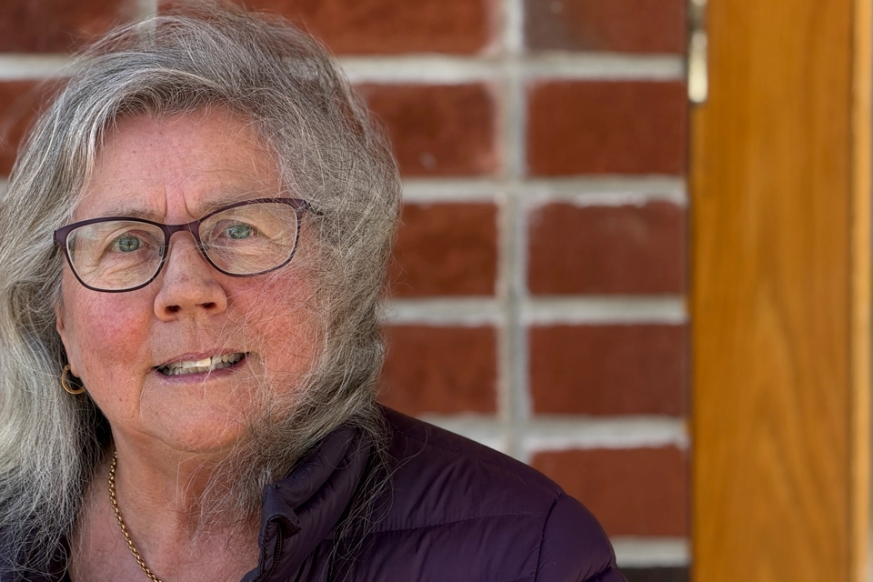 En kvinna med glasögon och en lila jacka.