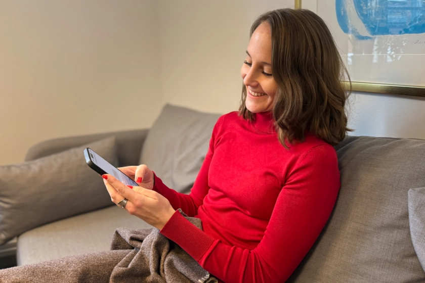 En kvinna sitter i en soffa och håller i en mobiltelefon.