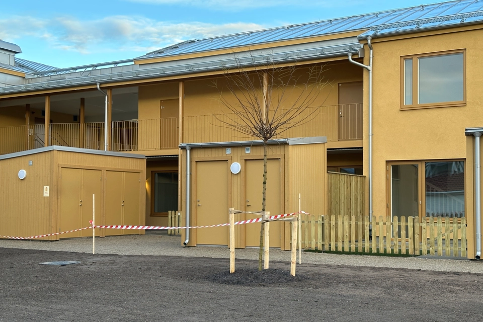 Visning av nybyggda bostäderna på Silvergatan, kvarteret Nötskrikan i Hemse. Flerfamiljshus i två våningar, gul fasad. Marken framför är bara tillplattad jord. Det är barmark men vinter. Klarblå himmel. 