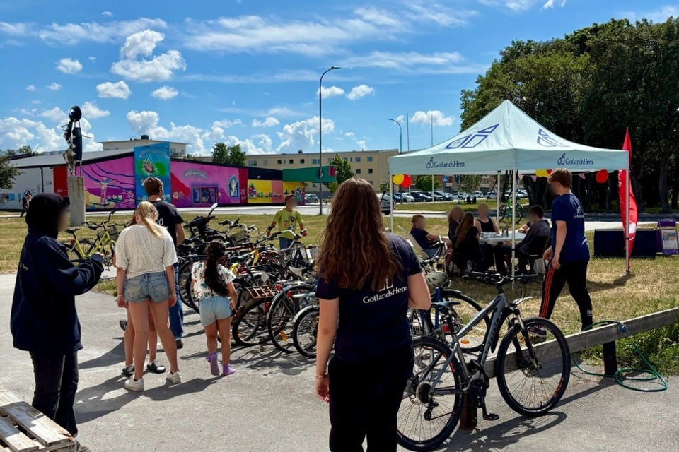 En grupp människor som står runt ett antal cyklar. Det finns ett stort blått tält som står "Gotlandshem" på.