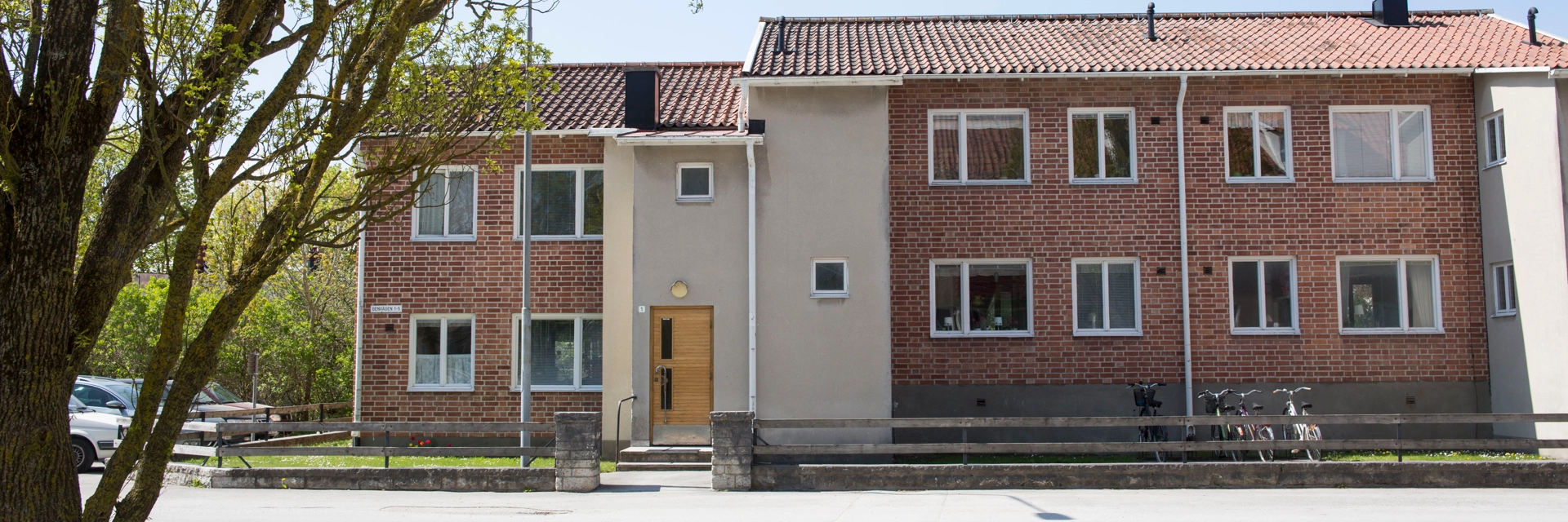Ett flerfamiljshus i rödbrunt tegel med vita detaljer. Himlen är blå.