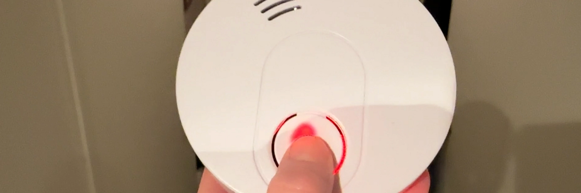 Ett finger trycker på testknappen på en brandvarnare.