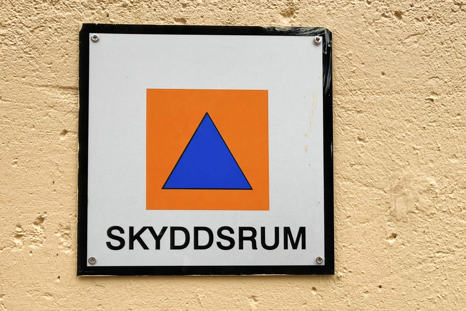 Skylt för hänvisning till skyddsrum som sitter på en gul vägg. 