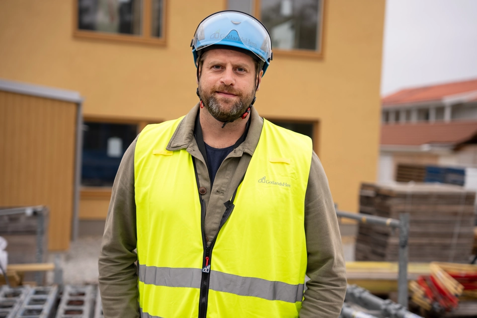 Projektledare Stefan Pettersson står framför en nyrenoverad bostad i varselväst och bygghjälm. 