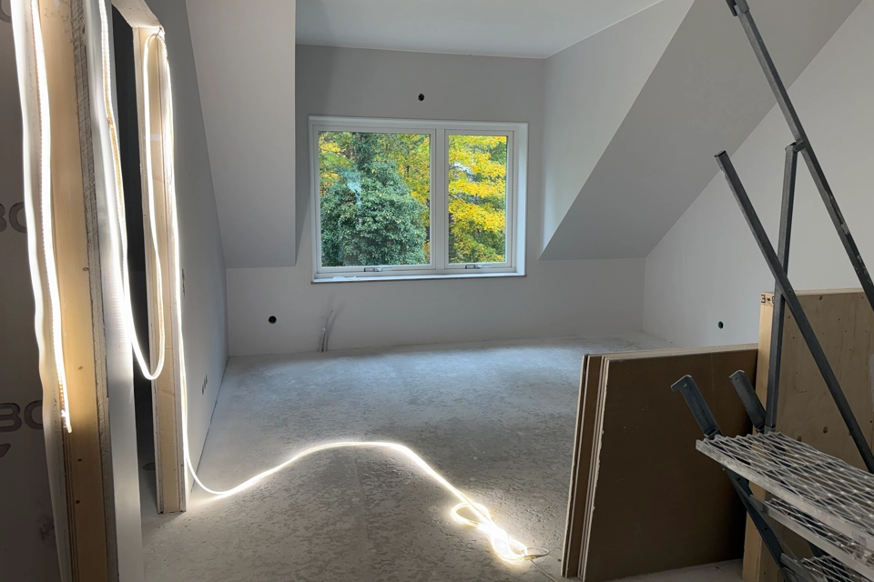 Ett tomt rum i en nybyggd bostad. Ett fönster ut om höstfärgade löv. Till höger en trappa upp till rummet.