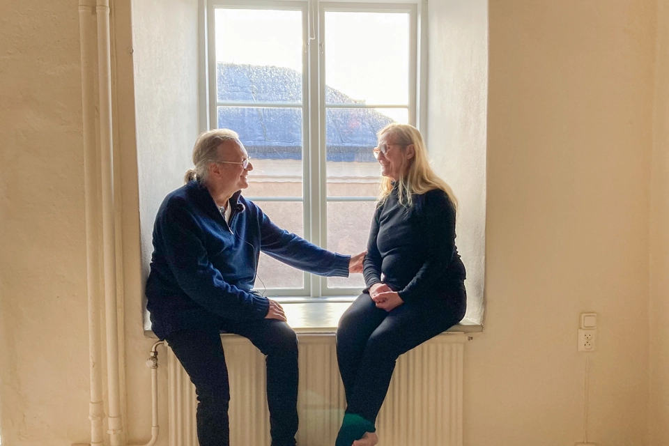 En man och en kvinna sitter tillsammans i ett fönster. Väggarna i rummet är vita.