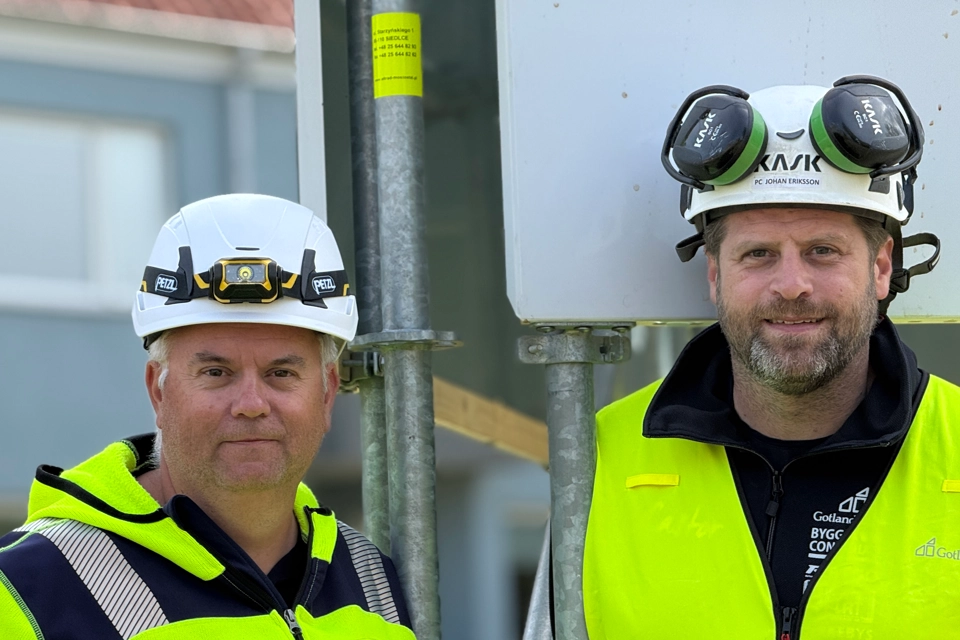 Två män i säkerhetsvästar som står bredvid en gatuskylt.