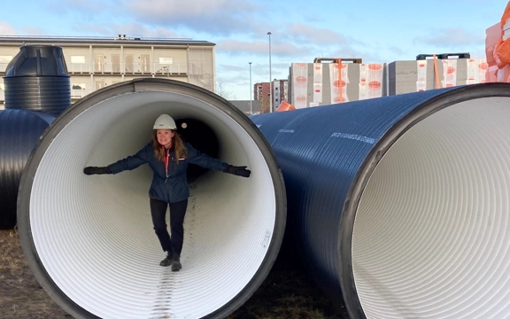 En kvinna med vit hjälm och blå GotlandsHem jacka står i en stor cylinderformad vattentank.